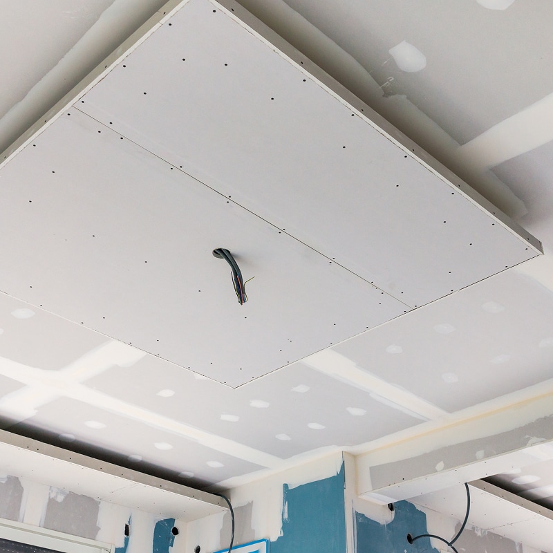 Plafond en plaques de placo lors d'un chantier de rénovation. Faux plafond central. Joints et vis enduits. Câble électrique pendant.