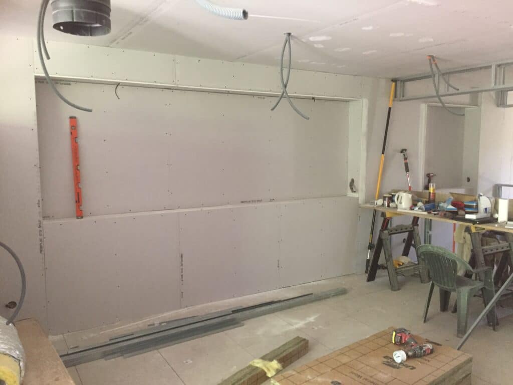 Pose de placo PREGYPLAC BA13 sur une cloison avec ouverture rectangulaire. Outillage de chantier, niveau et conduits électriques en attente.