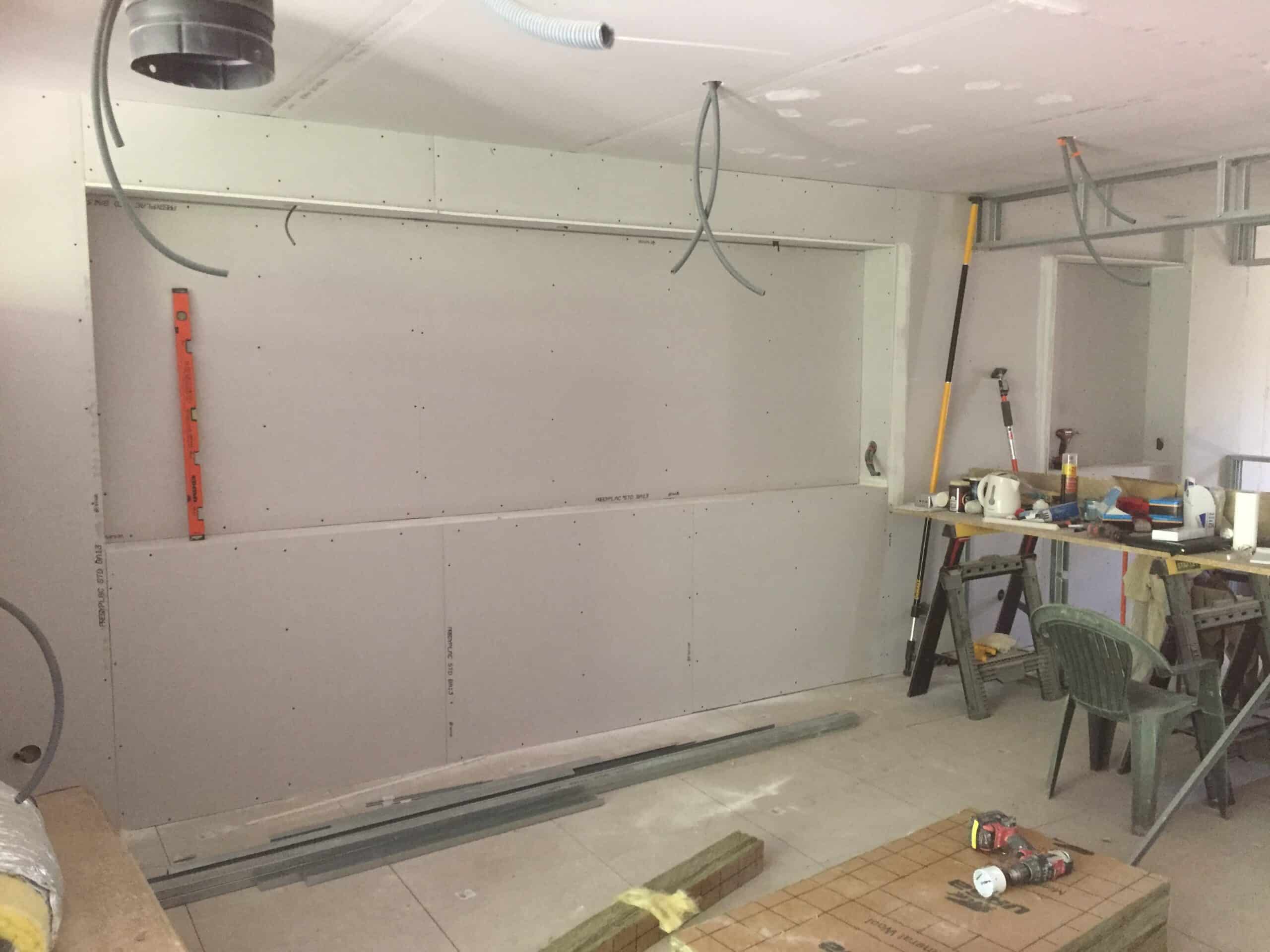 Plaque de plâtre BA13 : étapes de pose et rénovation intérieure. Pose de placo PREGYPLAC BA13 sur une cloison avec ouverture rectangulaire. Outillage de chantier, niveau et conduits électriques en attente.