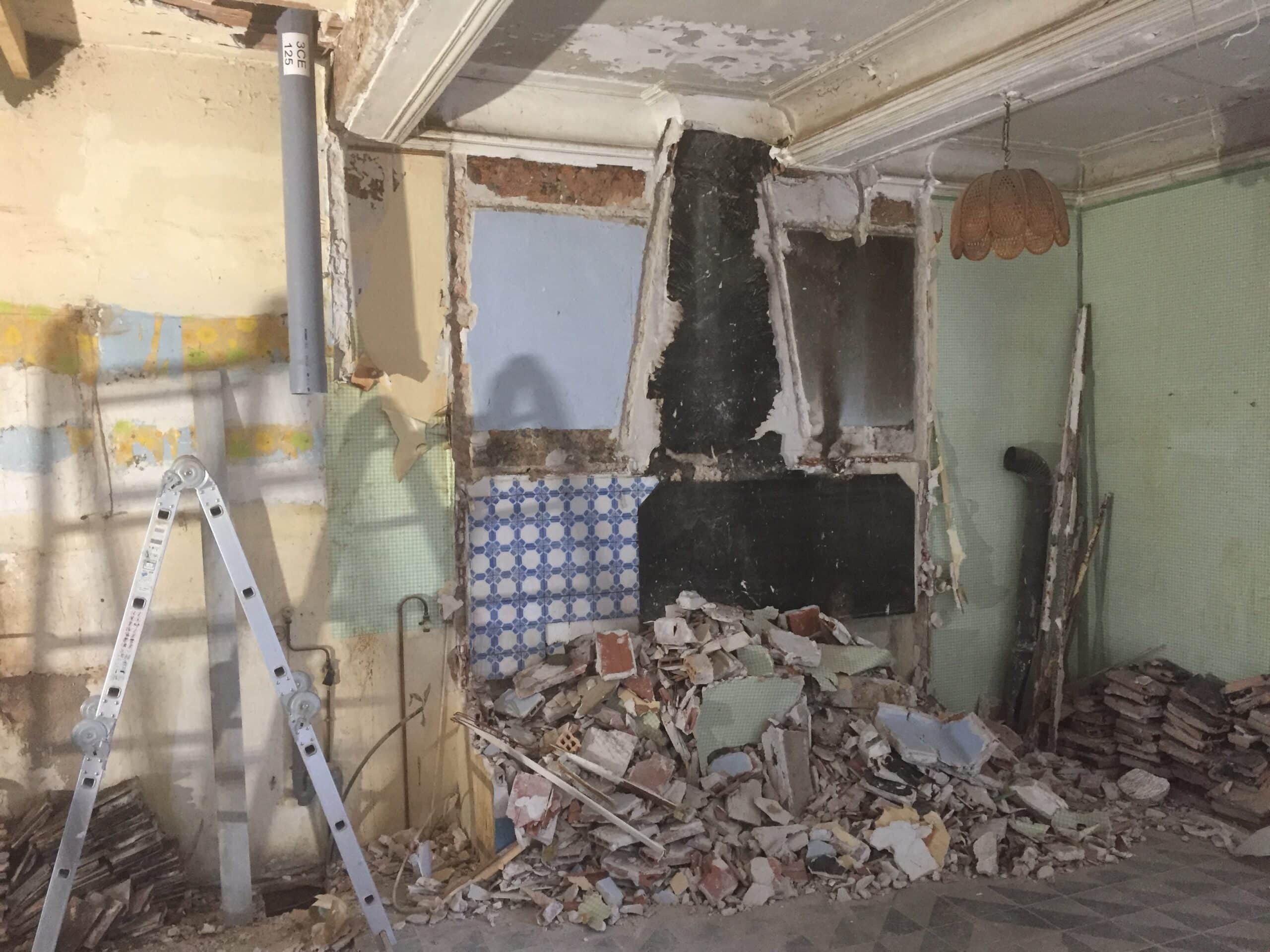Démolition et gravats : étape cruciale de la rénovation. Scène de chantier avec gravats, carreaux azulejos et ancienne cheminée murale démolie. Échelle alu et tuyau gris marqué 3CE 125.
