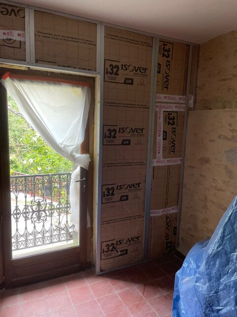 Isolation ISOVER pour rénovation : pose du doublage thermique Isolation thermique ISOVER 32 GR installée sur ossature métallique contre un mur en pierre, près d'une porte-fenêtre vitrée donnant sur un balcon.