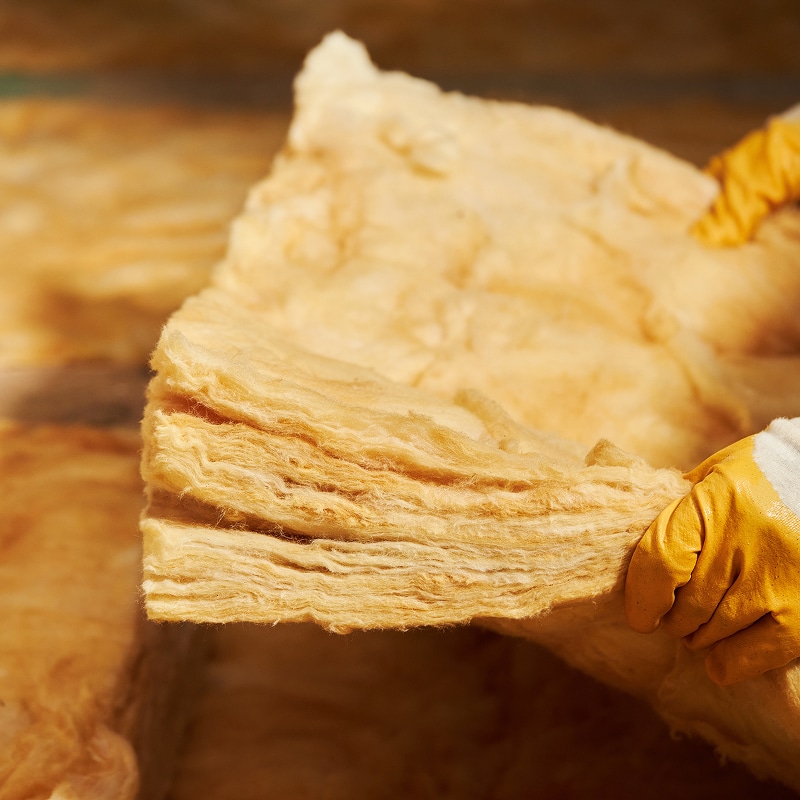 Pose de laine minérale pour une isolation thermique performante Main gantée tenant un rouleau épais de laine minérale (fibre de verre) pour l'isolation thermique lors de travaux de rénovation.