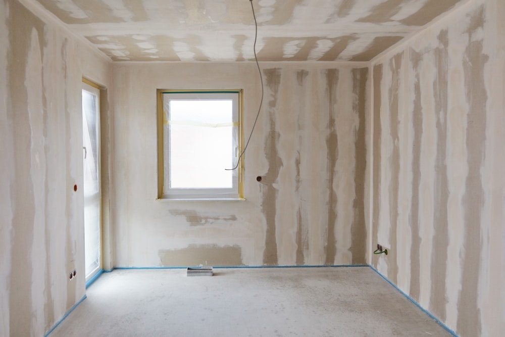 Rénovation Placo : Pièce vide en cours d'enduisage Intérieur vide en rénovation. Murs en plaques de plâtre avec bandes d'enduit de jointure visibles. Fenêtre protégée et sol brut.