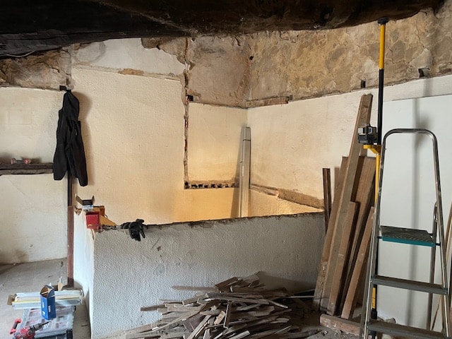 Rénovation rustique : murs, poutres en bois et chantier Intérieur en pleine rénovation : murs texturés et basse cloison, poutres sombres, échelle, laser de niveau et débris de bois.