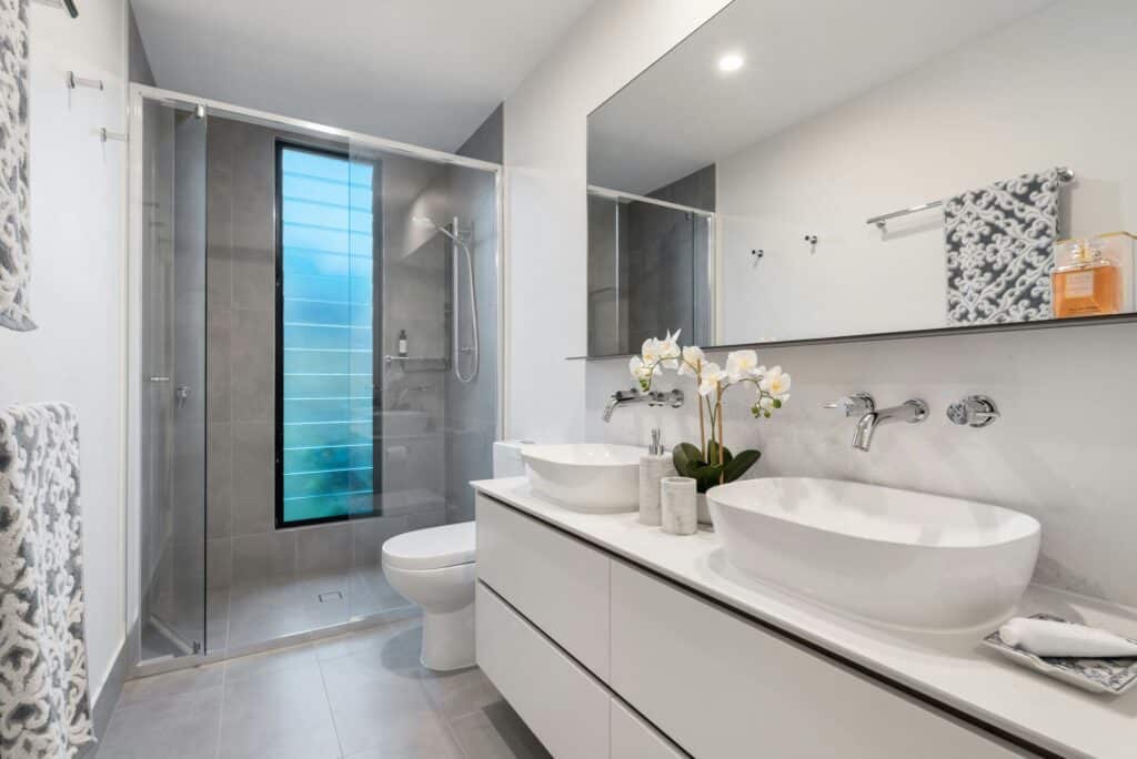 Salle de bain moderne de luxe : double vasque et douche vitrée Luxueuse salle de bain contemporaine: vanité blanche, double vasque, orchidée et douche vitrée minimaliste avec carrelage gris.