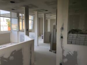 Chantier de rénovation intérieure montrant la pose de plaques de plâtre et cloisons sous une lumière naturelle vive.