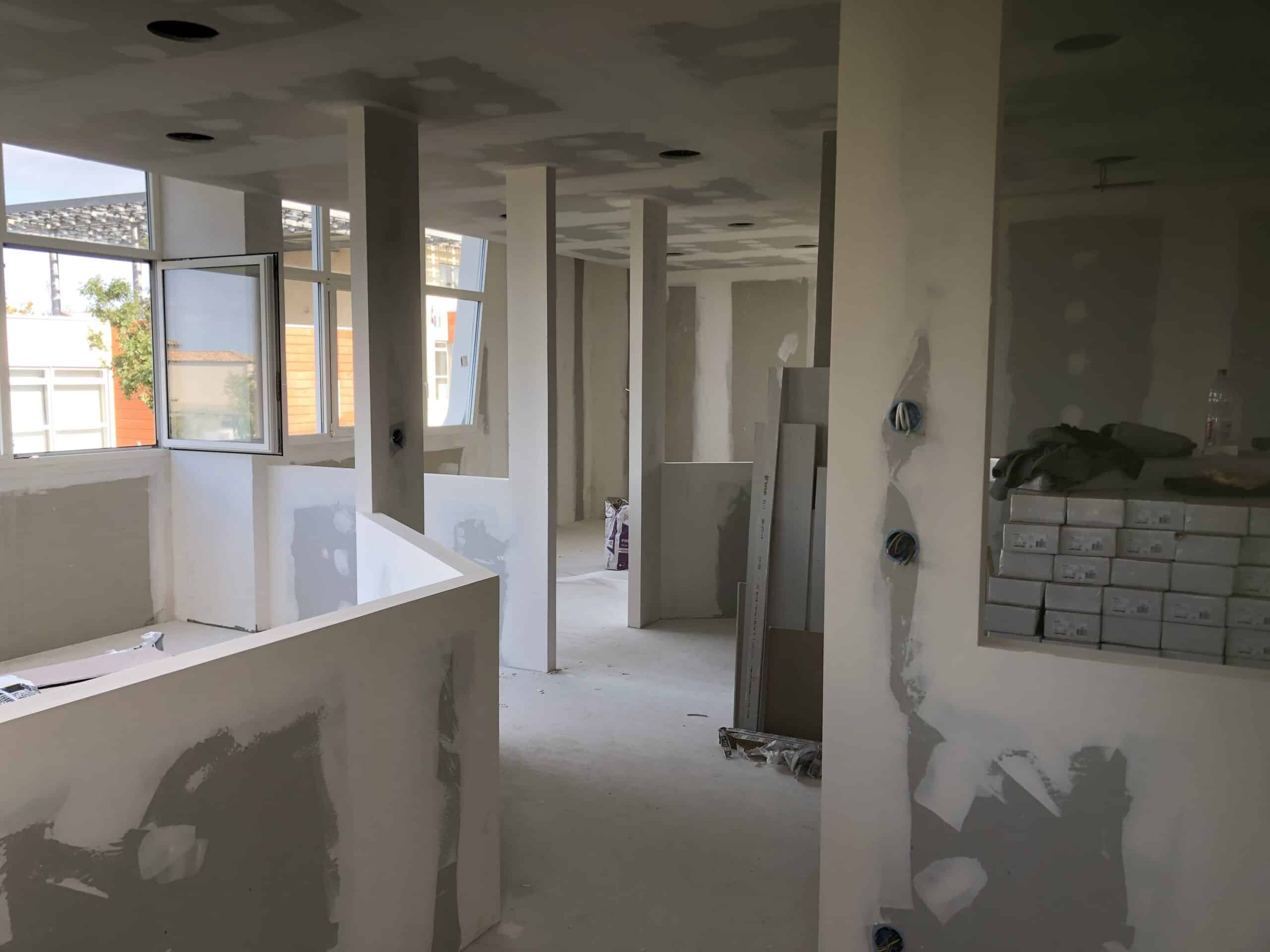 Chantier de rénovation intérieure montrant la pose de plaques de plâtre et cloisons sous une lumière naturelle vive.