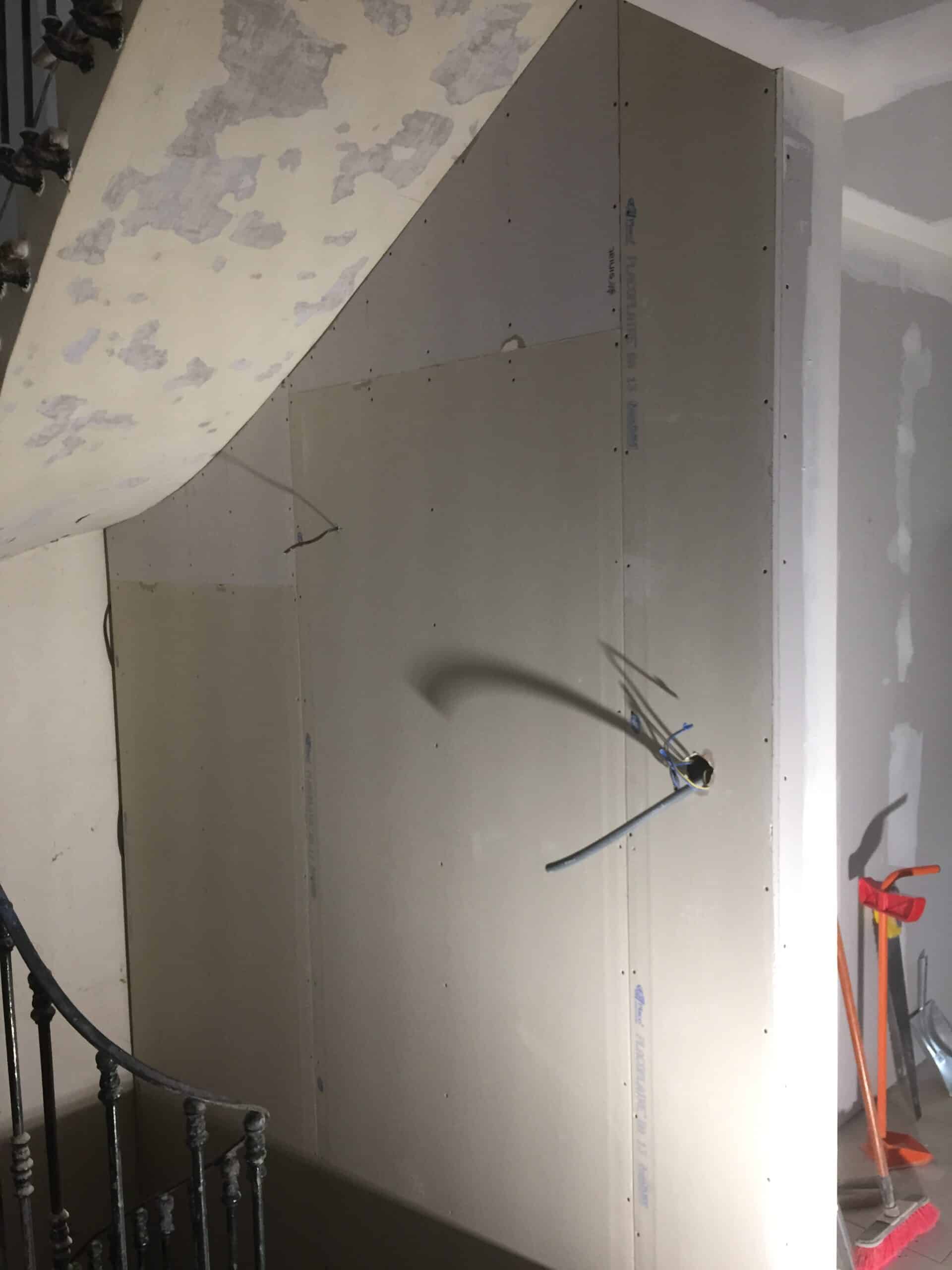 Cloison en plaques de plâtre BA 13 sous un escalier avec câblage électrique en cours de rénovation.