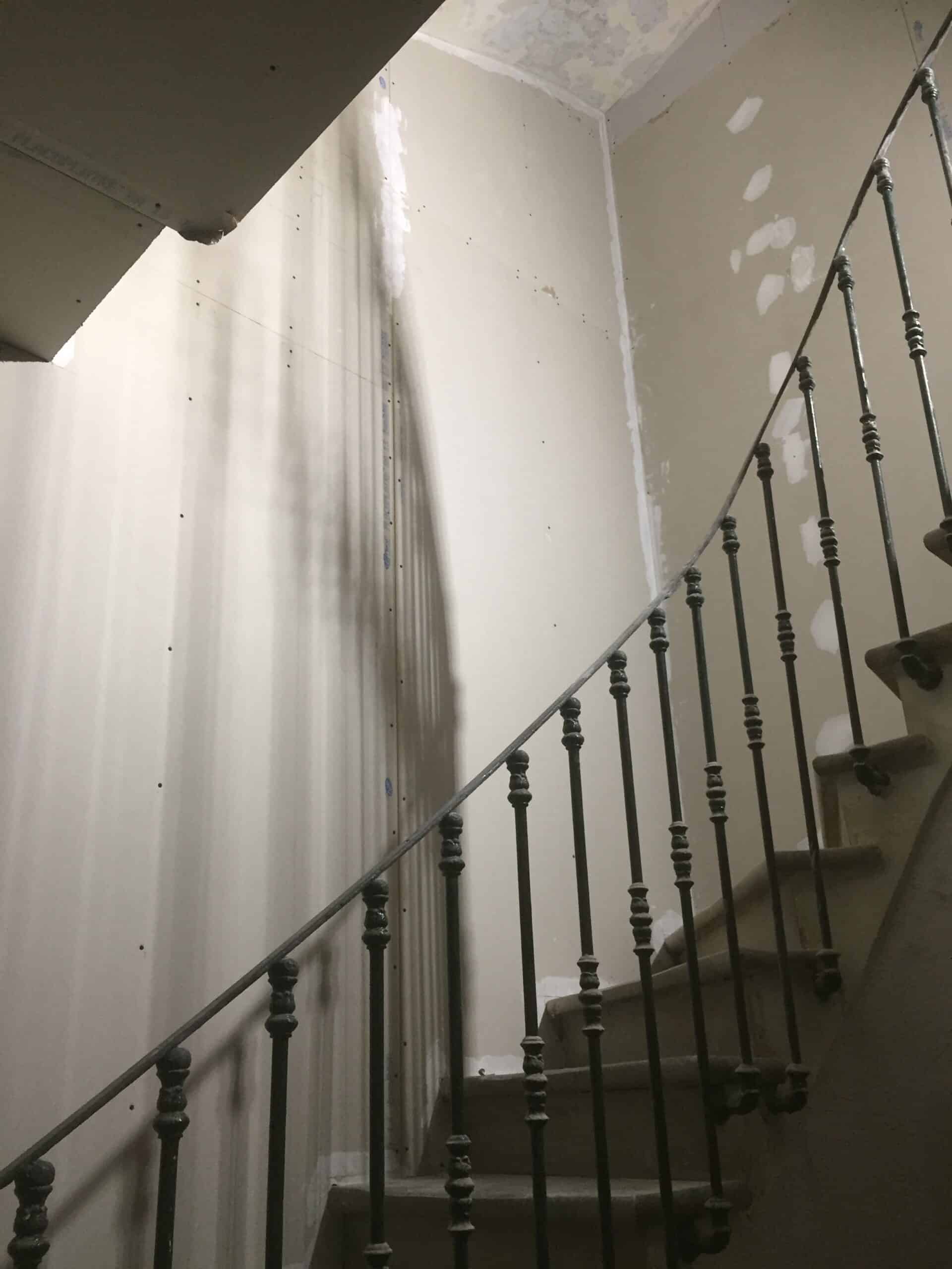 Garde-corps en fer forgé d'un escalier en rénovation avec murs en plaques de plâtre Placo et ombres portées.