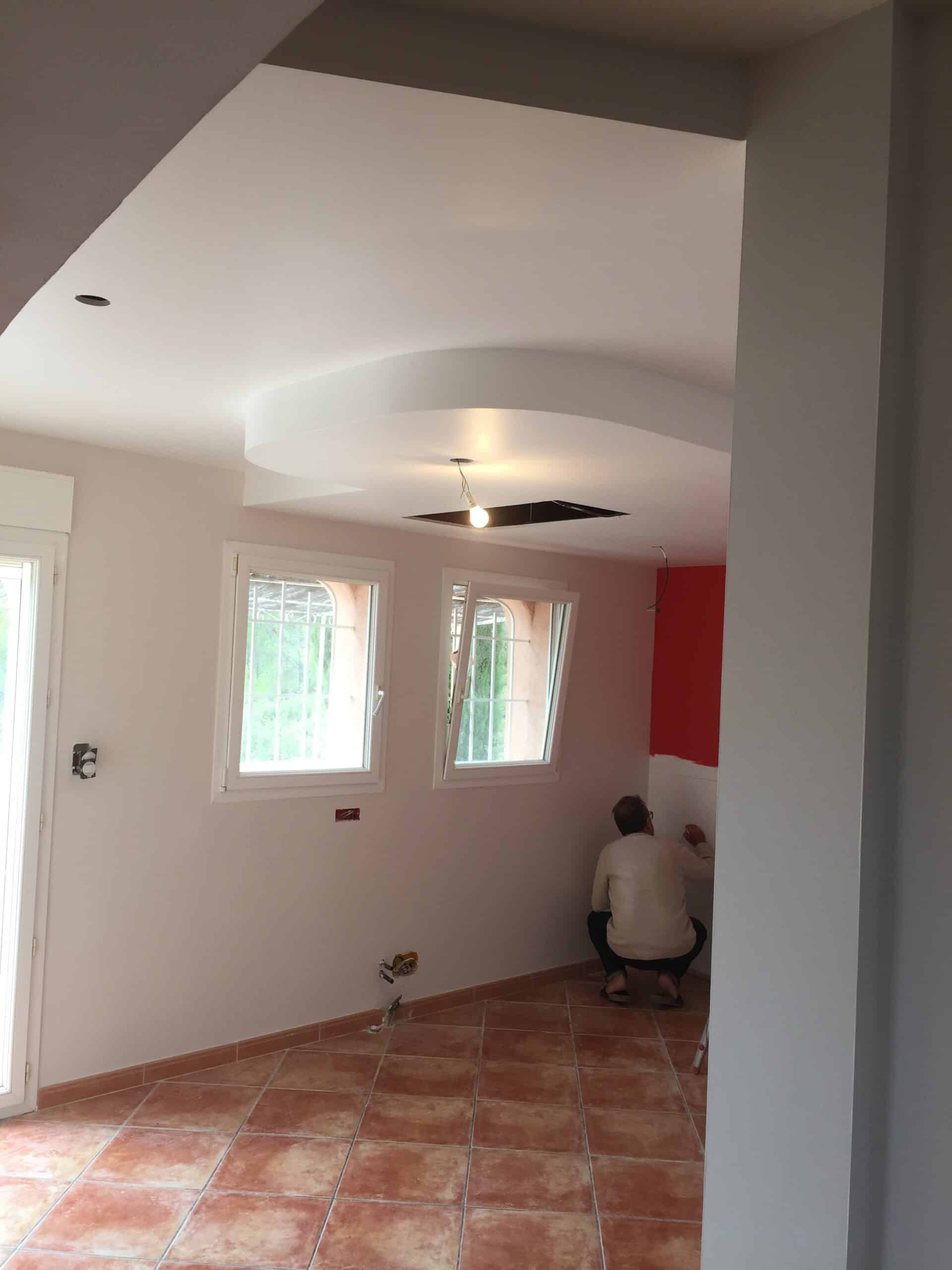 Un homme rénovant une pièce lumineuse dotée d'un plafond suspendu courbe et d'un sol en carrelage terre cuite.