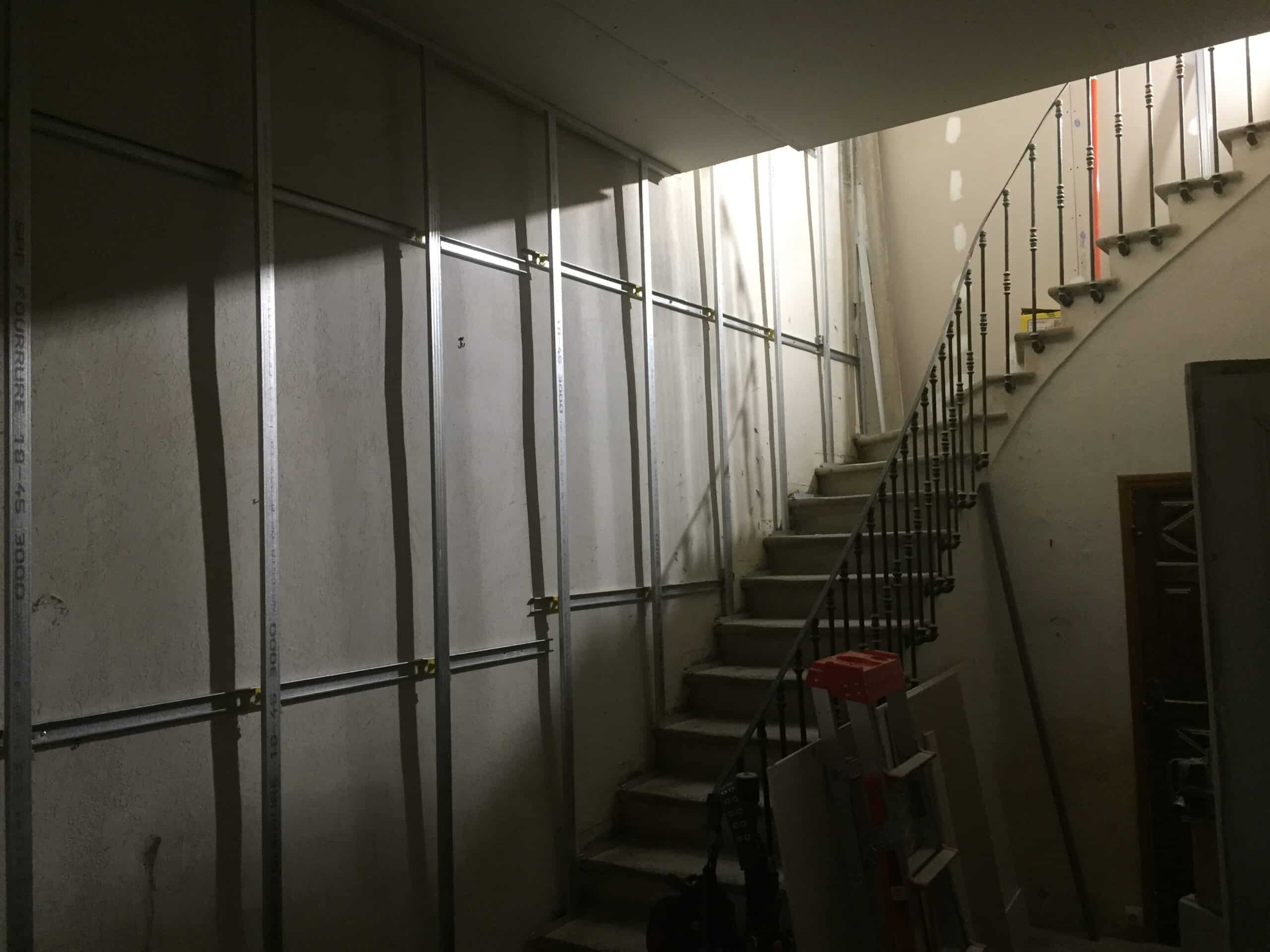 Ossature métallique SBF FOURRURE 18-45 installée sur un mur en rénovation à côté d'un escalier intérieur.